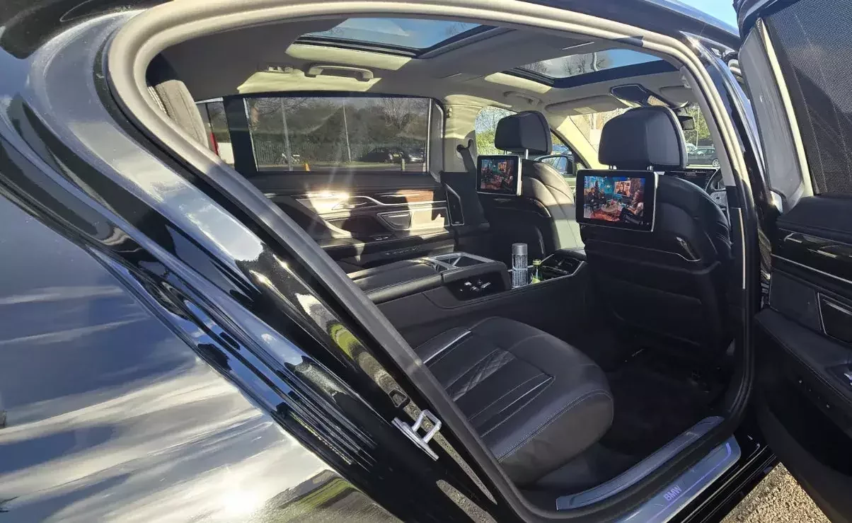 Luxury chauffeur vehicle interior showing spacious rear seating, individual entertainment screens, panoramic roof, and executive comfort features for premium passenger travel.